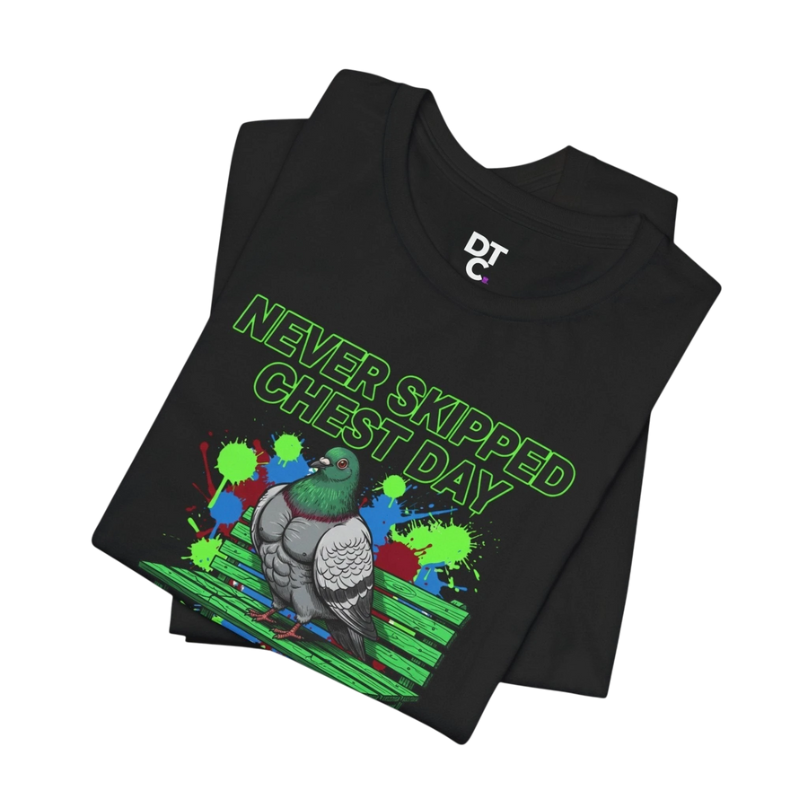 DailyThreadCo. black 100% cotton t-shirt with a graphic of a muscular pigeon on a green bench, with neon green text reading "NEVER SKIPPED CHEST DAY" and colorful paint splatters.