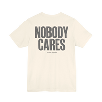 DailyThreadCo. cream cotton graphic t-shirt featuring Nobody Cares text on the back in a distressed grey font.