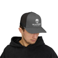 DailyThreadCo. grey and black trucker cap with a white skull logo, worn by a man in a black hoodie.