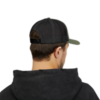 DailyThreadCo. olive green and black trucker cap with mesh back and adjustable snapback worn by a man in a hoodie.