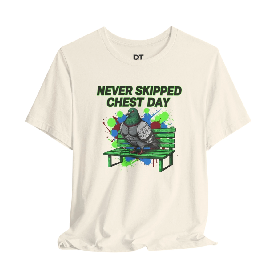 DailyThreadCo. cream cotton t-shirt with a graphic print of a muscular pigeon on a green park bench. Text reads "NEVER SKIPPED CHEST DAY".