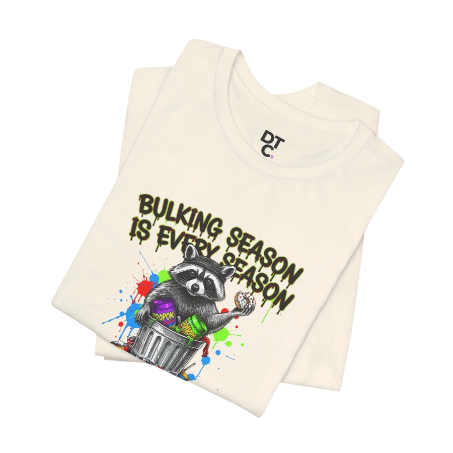 DailyThreadCo. cream 100% cotton t-shirt with a graphic of a raccoon in a trash can holding a donut, with the text "BULKING SEASON IS EVERY SEASON".