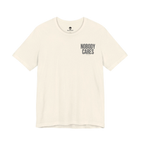 DailyThreadCo. Nobody Cares graphic tee in cream cotton with black chest text, featuring a crew neck and retail fit.