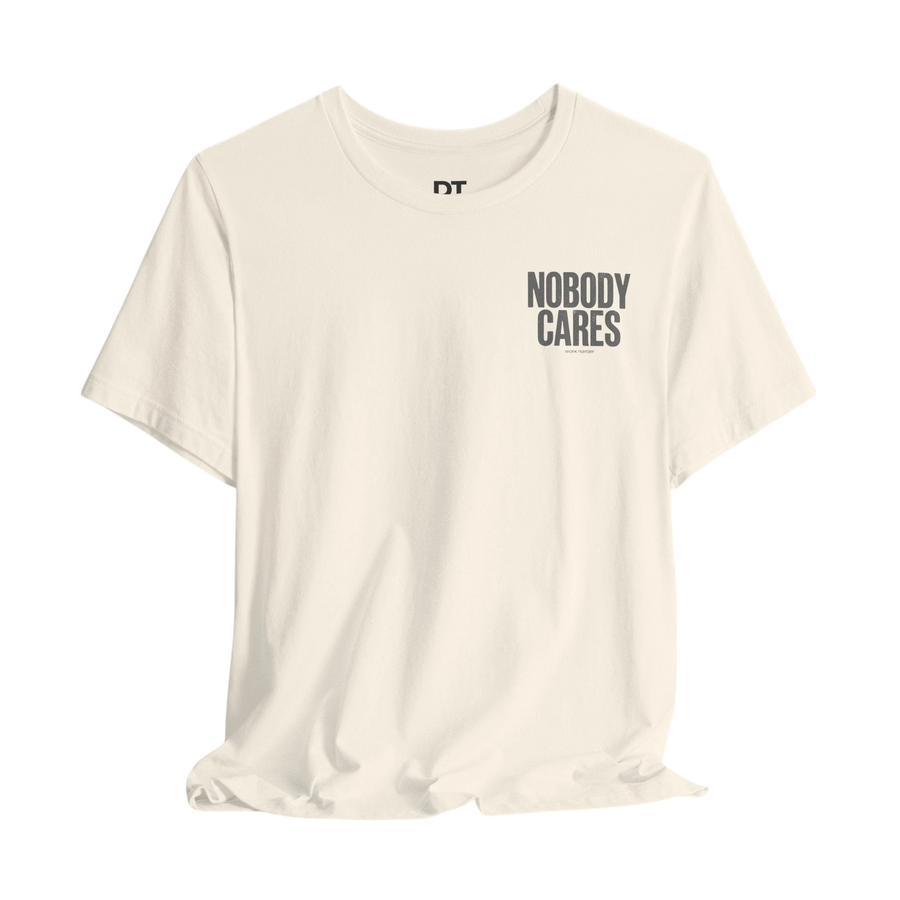 DailyThreadCo. cream 100% cotton graphic tee with "Nobody Cares" text art on the chest.
