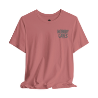 DailyThreadCo. Nobody Cares graphic tee in dusty rose cotton with a minimalist chest print and crew neckline.