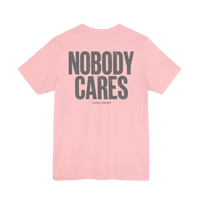 DailyThreadCo. pink cotton graphic t-shirt with Nobody Cares text printed on the back in a distressed grey font.