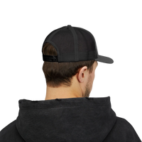 DailyThreadCo. black trucker cap with mesh back and adjustable snap closure worn by a man in a dark hoodie.