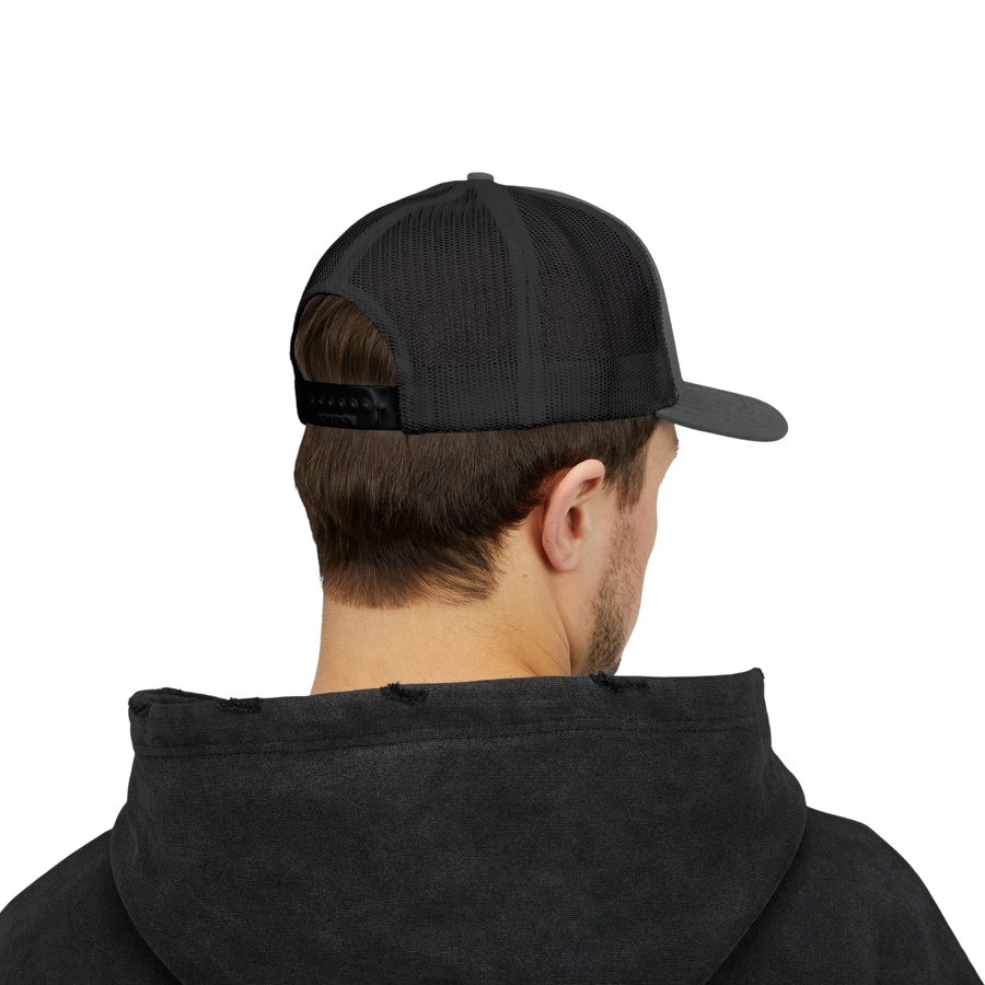 DailyThreadCo. black trucker cap with mesh back and adjustable snap closure worn by a man in a dark hoodie.