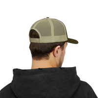DailyThreadCo. olive green and tan mesh back trucker cap with adjustable snapback worn by a man in a black hoodie.